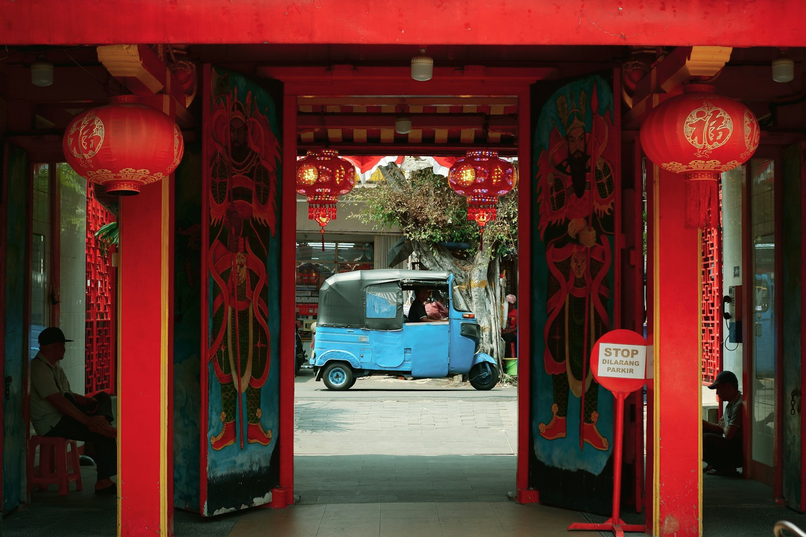 Blue tuk-tuk drives through red ornate gateway